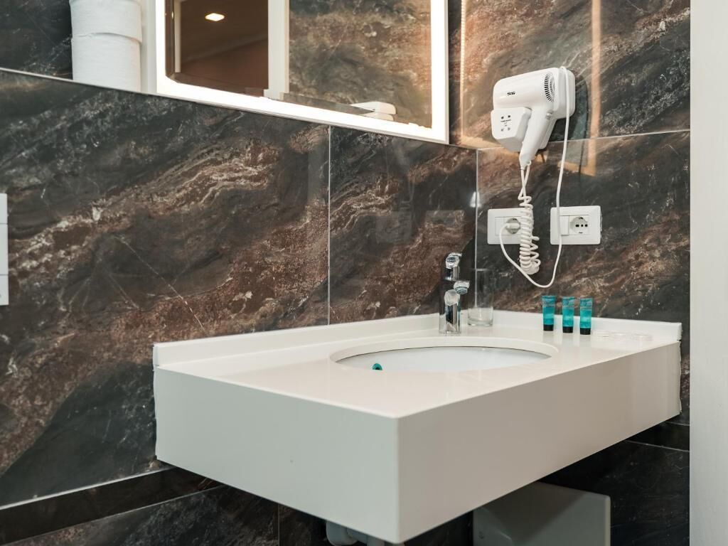 A modern bathroom with a white sink, a hairdryer mounted on the wall, and a mirror above the sink.