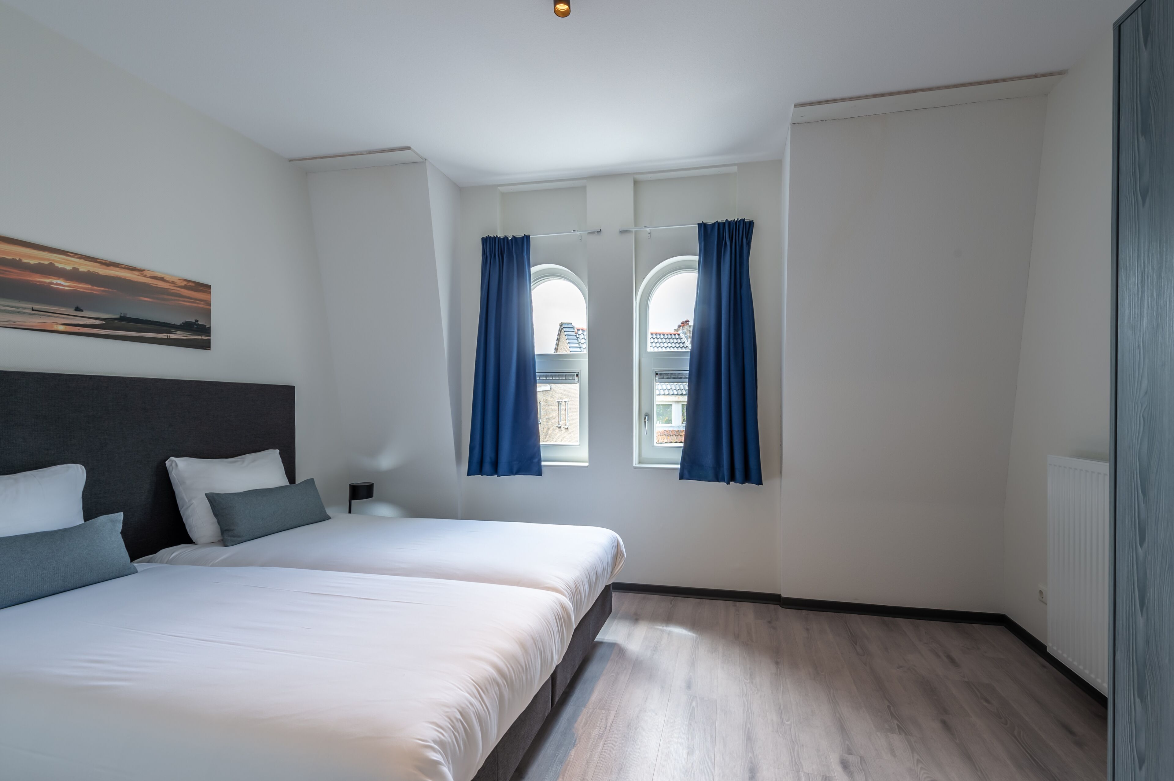 Habitación de hotel moderna con dos camas, un ventanal con cortinas y vistas a la ciudad, además de un radiador en la pared.