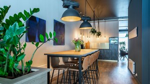 Cozinha moderna com mesa de madeira, banquetas, iluminação pendente e plantas suspensas.