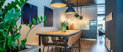 A modern kitchen with a wooden table, bar stools, pendant lighting, and hanging plants.