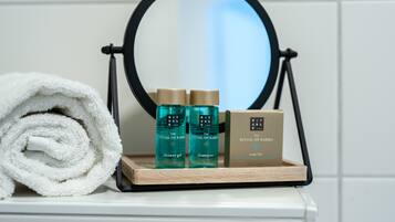 A bathroom vanity with a mirror, a towel, and a tray holding a shower gel bottle, a shampoo bottle, and a soap bar.