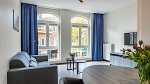 Quarto de hotel moderno com sofá, mesa de jantar e televisão.