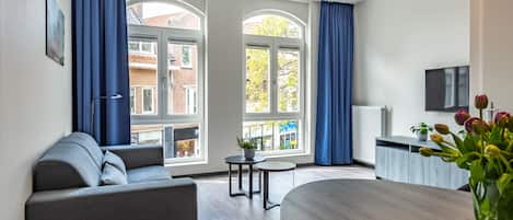 Ein modernes Hotelzimmer mit einer Couch, einem Esstisch und einem Fernseher.