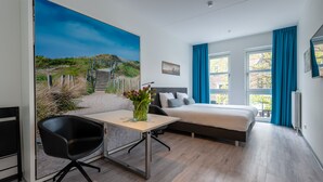 Quarto de hotel moderno com uma cama, uma mesa e uma cadeira. Há um quadro com uma cena de praia na parede.