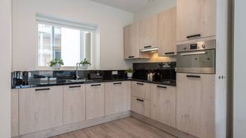 A modern kitchen with light wood cabinets, black countertops, and stainless steel appliances.