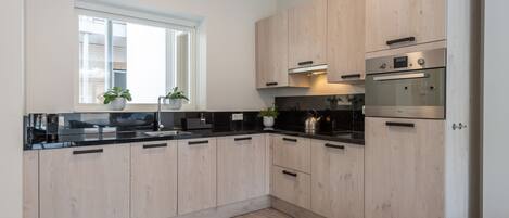 A modern kitchen with light wood cabinets, black countertops, and stainless steel appliances.