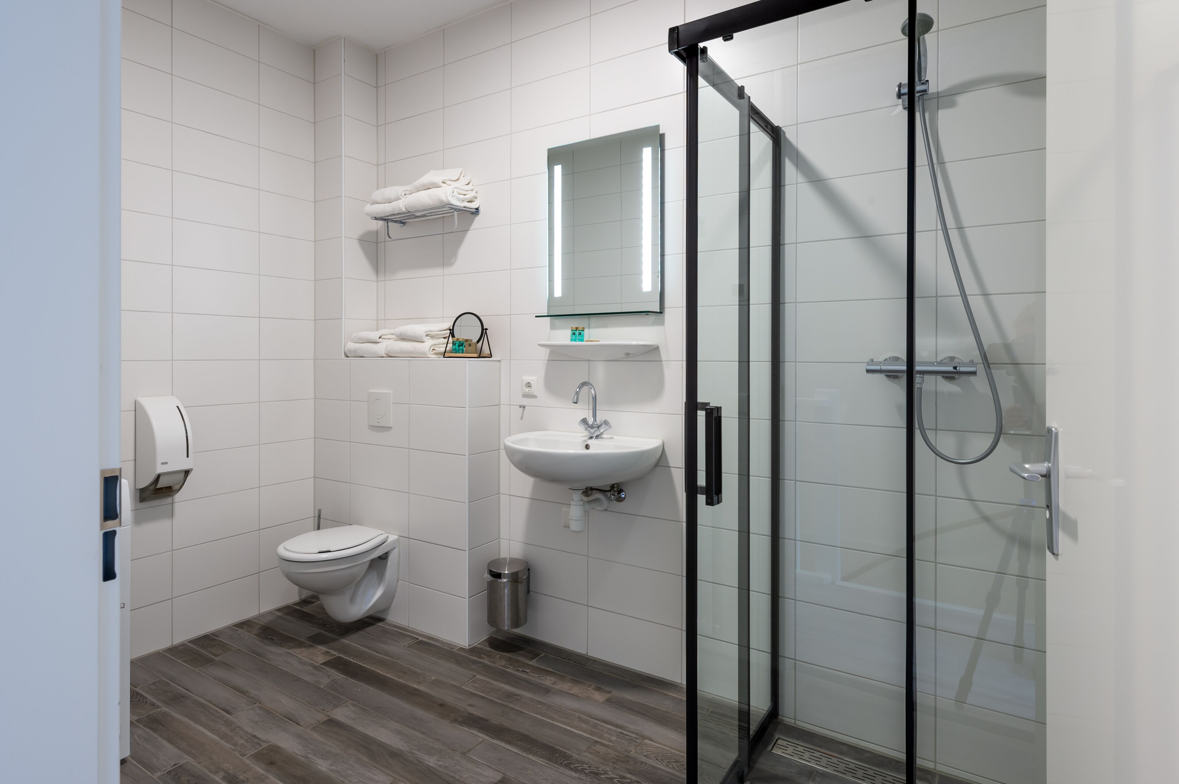 Een moderne badkamer met een douchecabine van glas, een witte wastafel en een toilet.