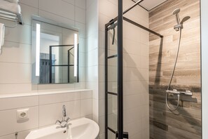 Une salle de bain moderne avec une douche à l’italienne en verre, un lavabo blanc et un grand miroir.