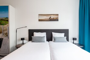 Une chambre d’hôtel avec deux lits, un tableau représentant une scène de plage et une vue sur la plage depuis une porte ouverte.