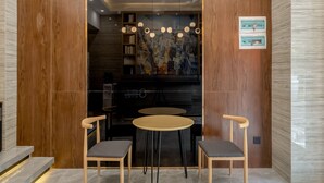 A modern interior with a wooden wall, a black piano, two round tables with chairs, and a ceiling light fixture.