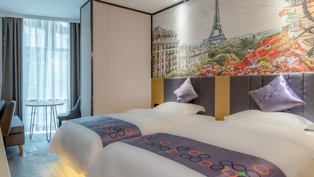 A hotel room with a large bed, a desk, and a chair. There is a painting of the Eiffel Tower on the wall.