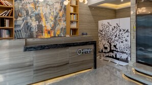 A modern reception desk with a cityscape mural, wooden shelving with books, and a decorative panel with birds.