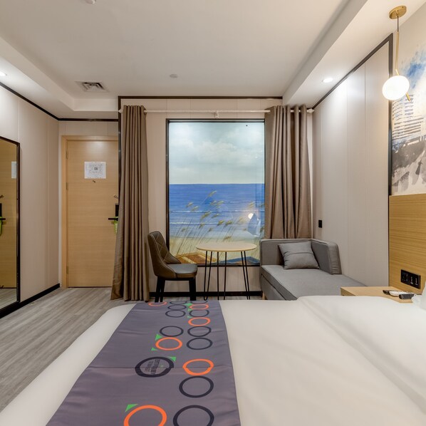 Une chambre d’hôtel avec un lit, un bureau et une chaise, un canapé, une fenêtre donnant sur la mer et une affiche accrochée au mur.