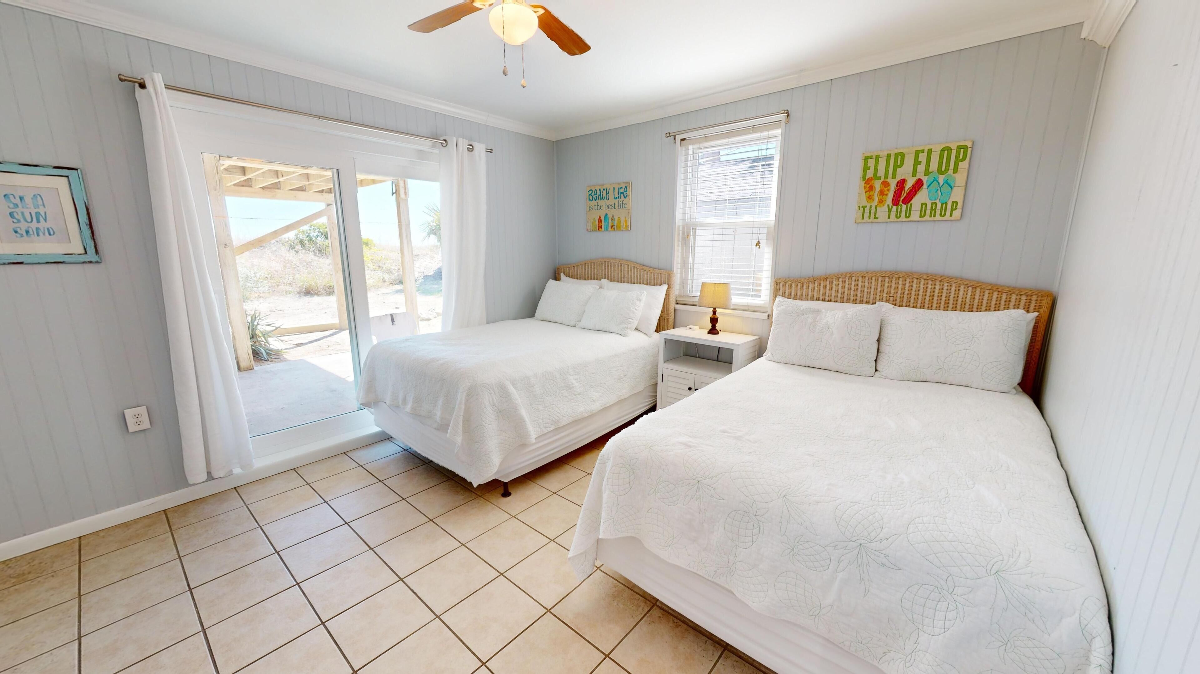 A bedroom with two beds, a ceiling fan, and a window with blinds.