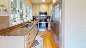 Una cocina con encimeras de granito, electrodomésticos de acero inoxidable y vistas al exterior a través de amplios ventanales.