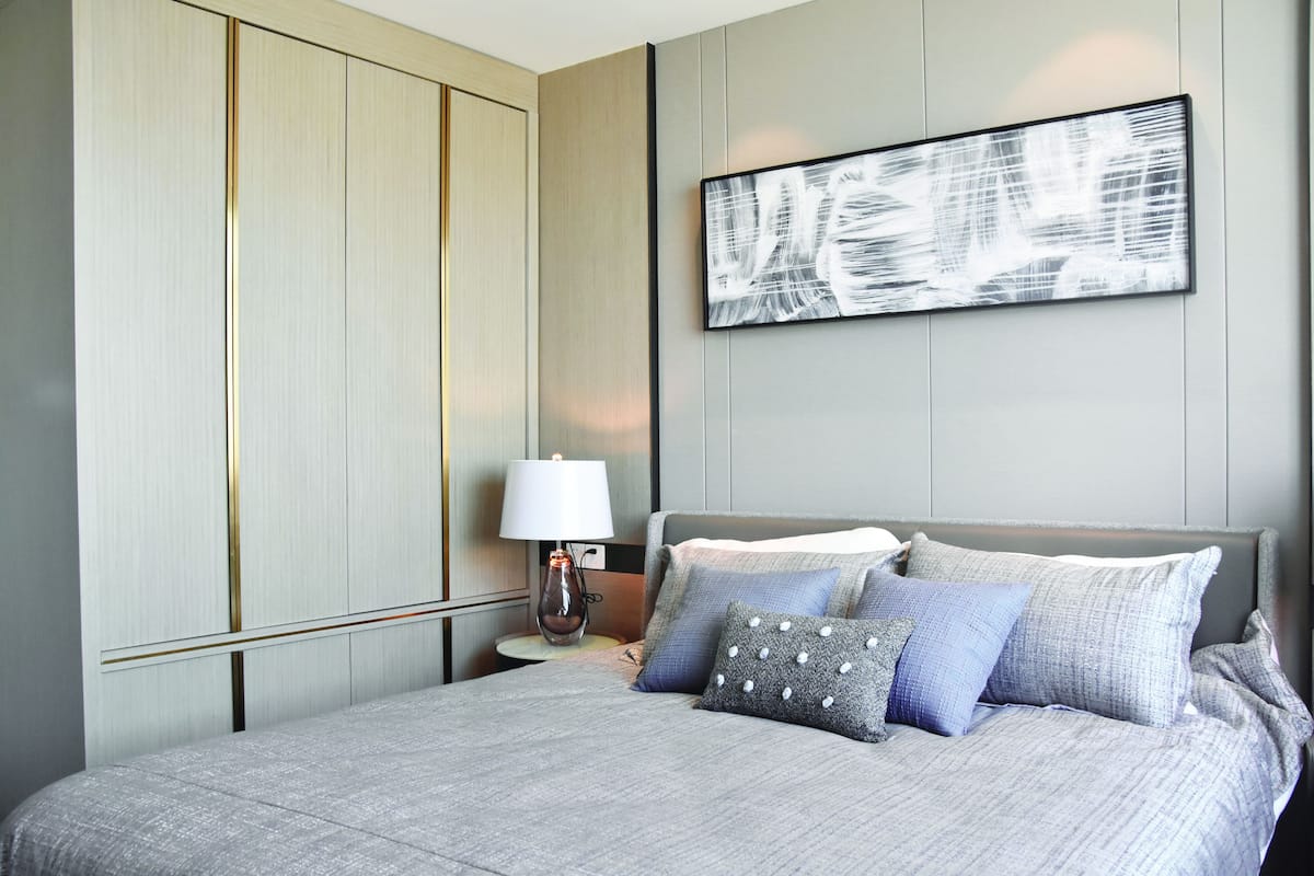A modern bedroom with a large bed, a bedside table with a lamp, and a wall-mounted abstract painting.