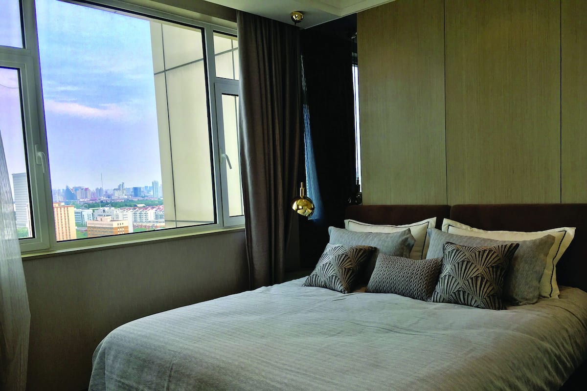 A hotel room with a large bed, a view of a cityscape through a window, and a curtain on the window.