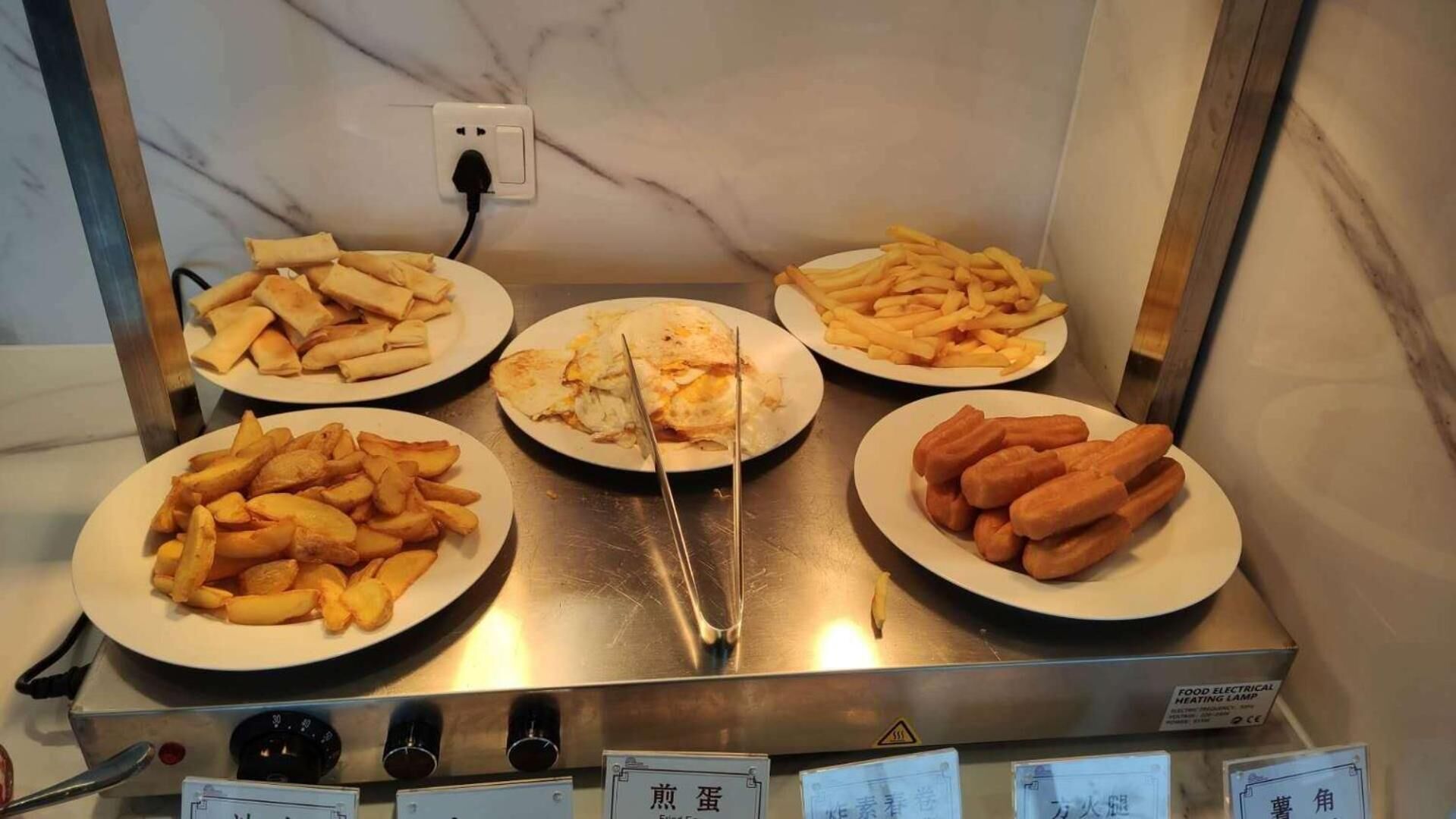 A buffet with plates of French fries, spring rolls, and other fried items.