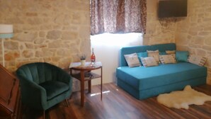 A room with a stone wall, a teal sofa with patterned cushions, a small wooden table with a bottle and a plant, a green armchair, and a white fur rug on the floor. - Boutique Villa Marijini Dvori (Tribunj)