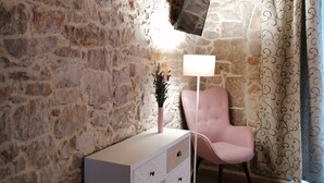 A room with a stone wall, a white dresser, a pink chair, a floor lamp, and a flat-screen TV mounted on the wall. - Boutique Villa Marijini Dvori (Tribunj)