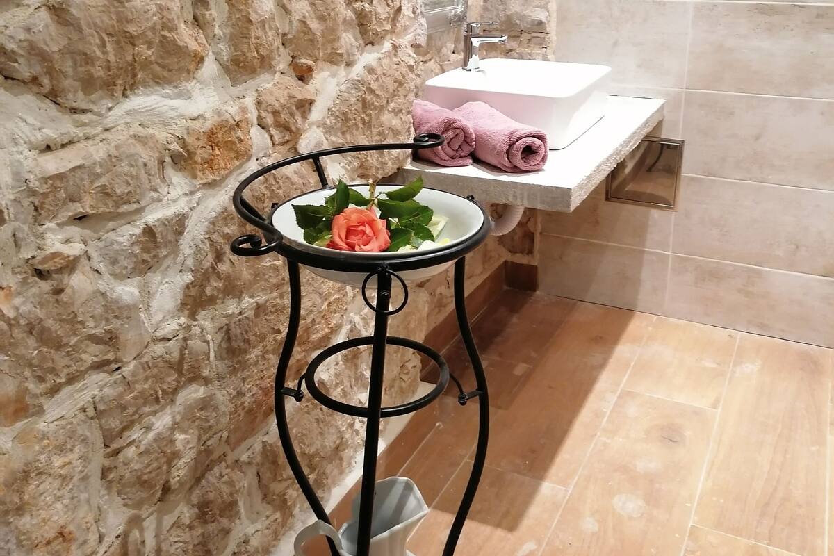 A bathroom with a stone wall, a sink, and a small table with a flower.