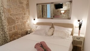 A neatly made bed with white linens and a pink towel, a stone wall, a mirror, and bedside lamps. - Boutique Villa Marijini Dvori (Tribunj)
