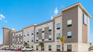 Un hotel moderno con techo plano, múltiples ventanas y un estacionamiento con varios coches.