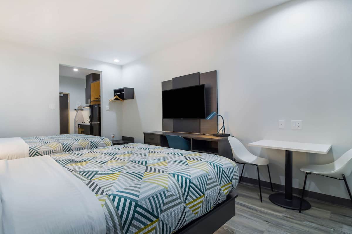 A modern hotel room with two beds, a desk, a chair, a TV, and a small table.