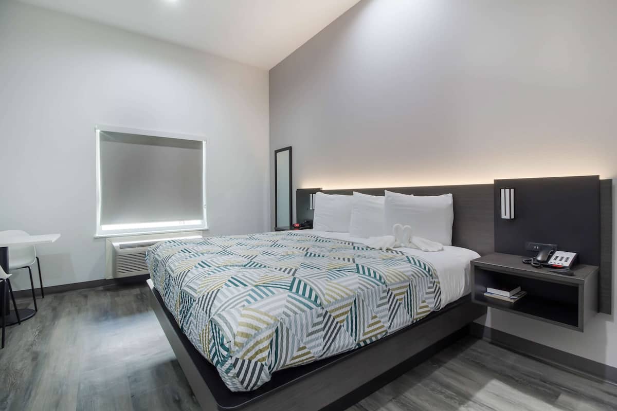 A modern hotel room with a large bed, bedside table, and a desk.