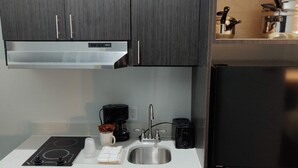 Una cocina compacta con armarios de madera oscura, un lavamanos de acero inoxidable, un refrigerador negro, un microondas y una cafetera.