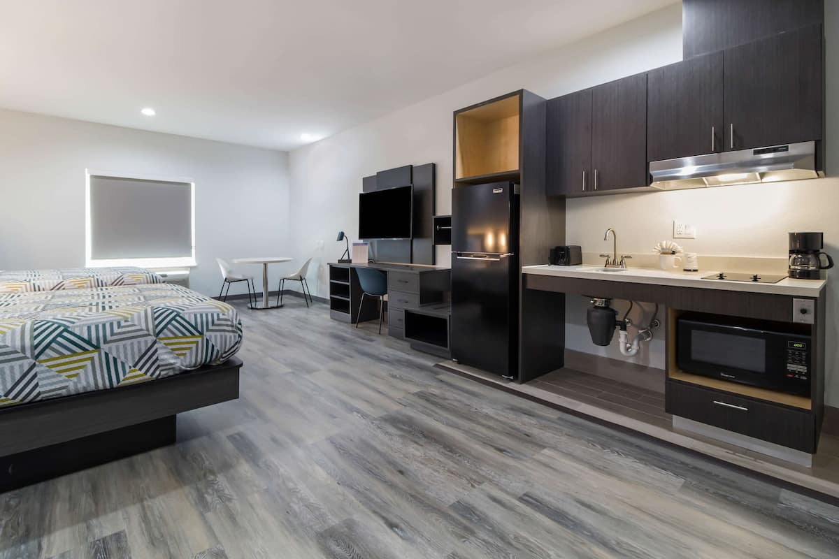 A modern hotel room with a bed, a desk, a flat-screen TV, a built-in refrigerator, a microwave, and a coffee maker.