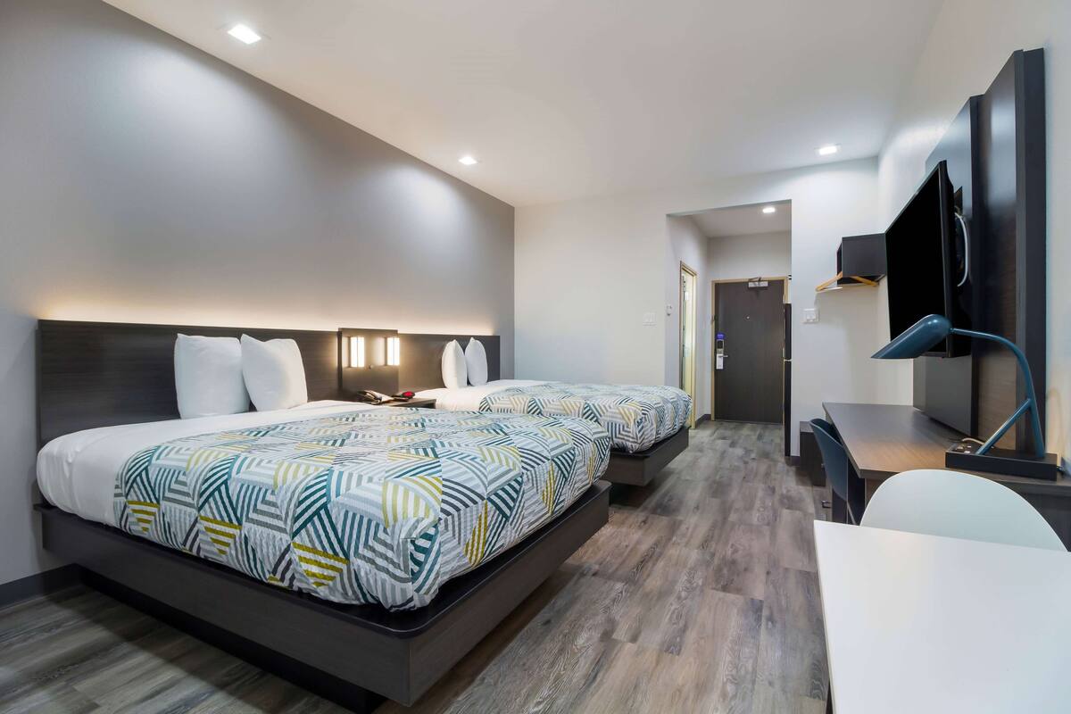 A modern hotel room with two beds, a desk, a chair, and a TV.