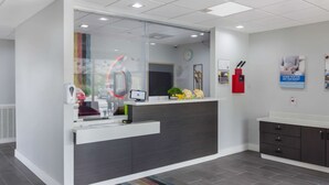 Una zona de recepción moderna con un separador de vidrio, un mostrador de recepción, un reloj y un extintor rojo.