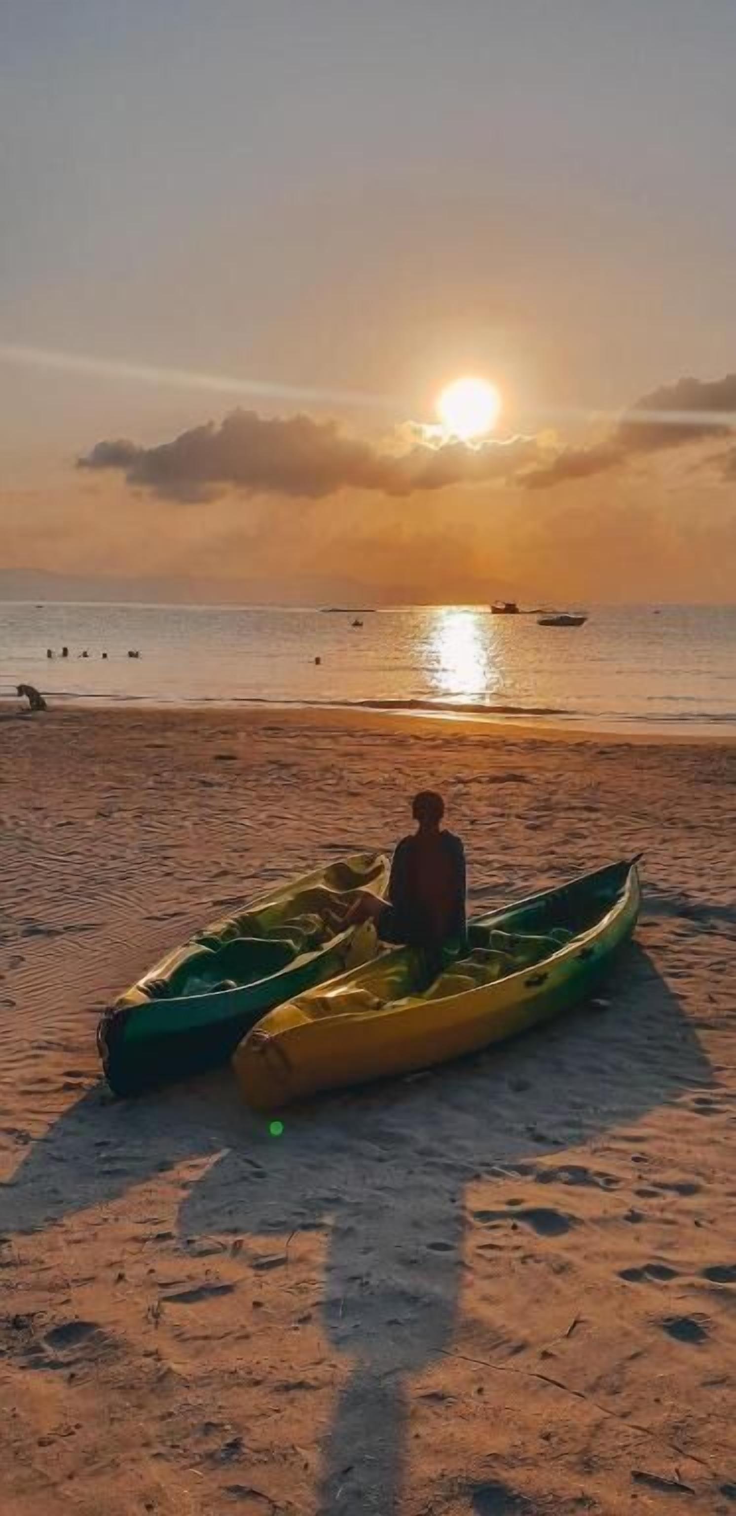 A beach scene with a person standing next to a green and yellow kayak.