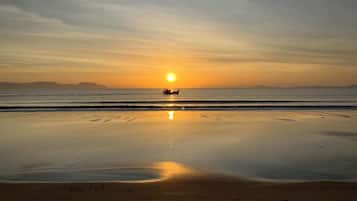 A beach at sunset with calm waters and a boat in the distance.