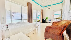Habitación de hotel con cama, una silla de mimbre, una mesita y ventana con vista al mar.