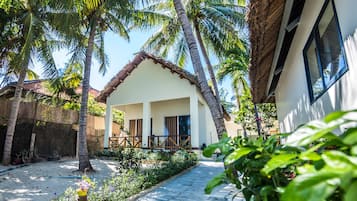 Uma cabana com telhado de palha, cercada por palmeiras e um jardim.