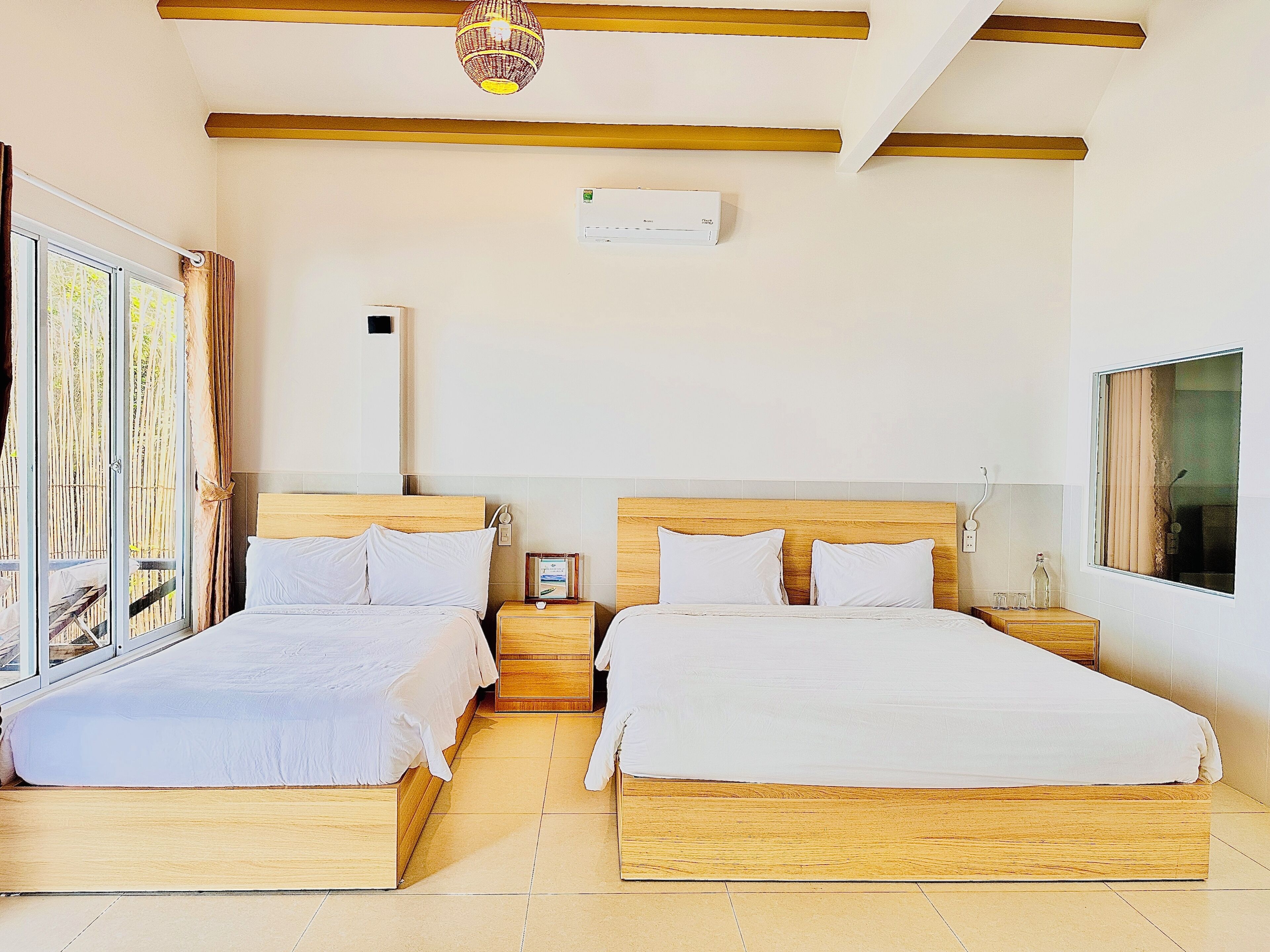 A hotel room with two wooden beds, a ceiling fan, a window with curtains, and a wall-mounted air conditioning unit.