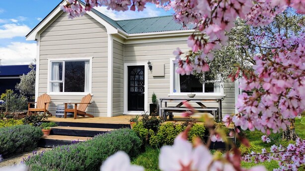 A two-story house with a front porch, a small deck, and a garden with various plants and flowers. - Olive Tree Cottage, Martinborough (Martinborough)
