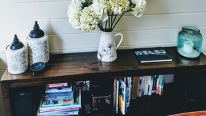 A mirror on a wall, a vase with flowers, two decorative jars, a book, and a glass jar on a wooden table. - Olive Tree Cottage, Martinborough (Martinborough)