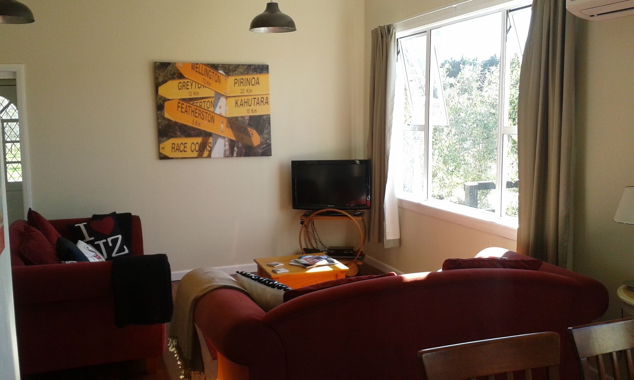 A living room with a red sofa, a television on a stand, and a wall sign with directional distances to various locations.