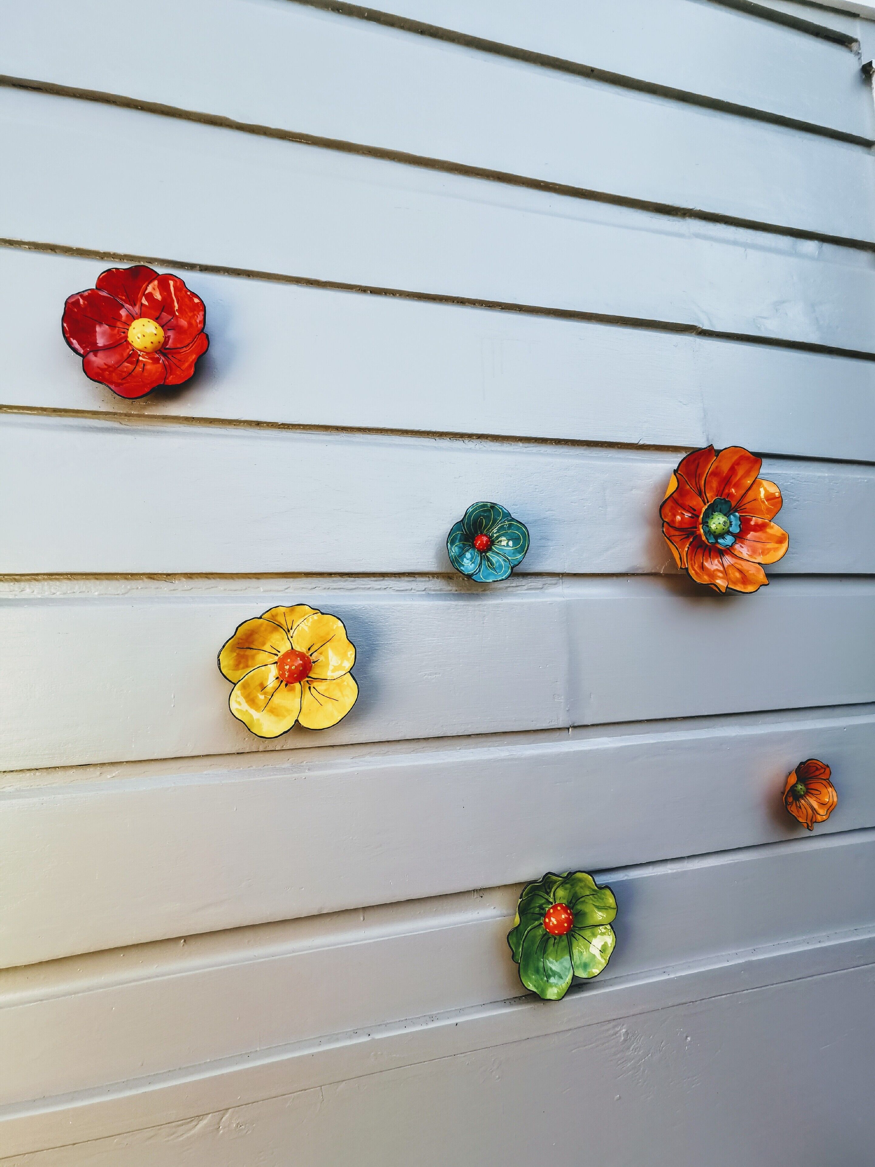 Un mur composé de planches de bois disposées horizontalement et agrémenté de boutons décoratifs en forme de fleurs, déclinés dans différentes couleurs.