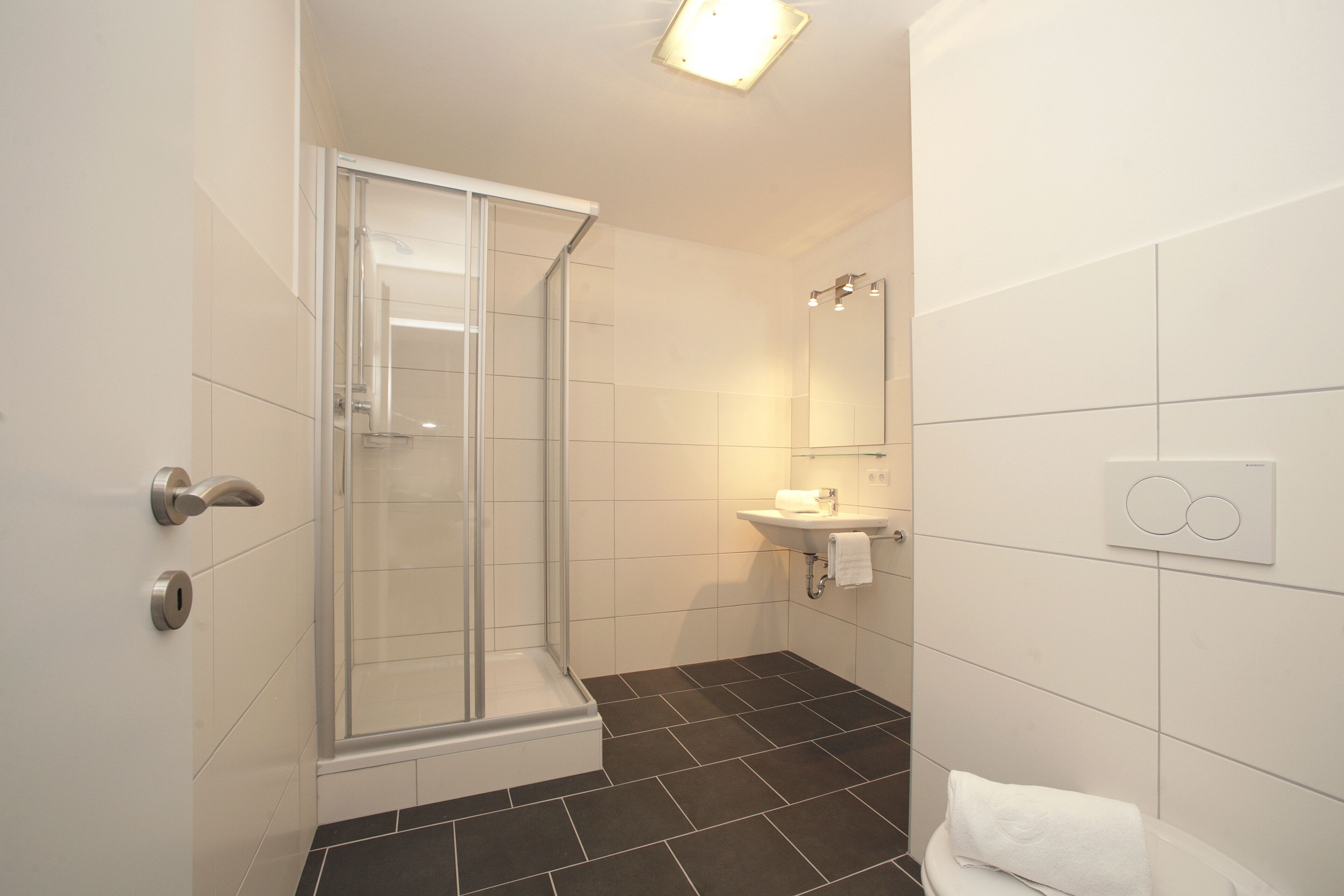 Ein modernes Badezimmer mit einer gläsernen Duschkabine, einem weißen Waschbecken und einem Handtuchhalter.
