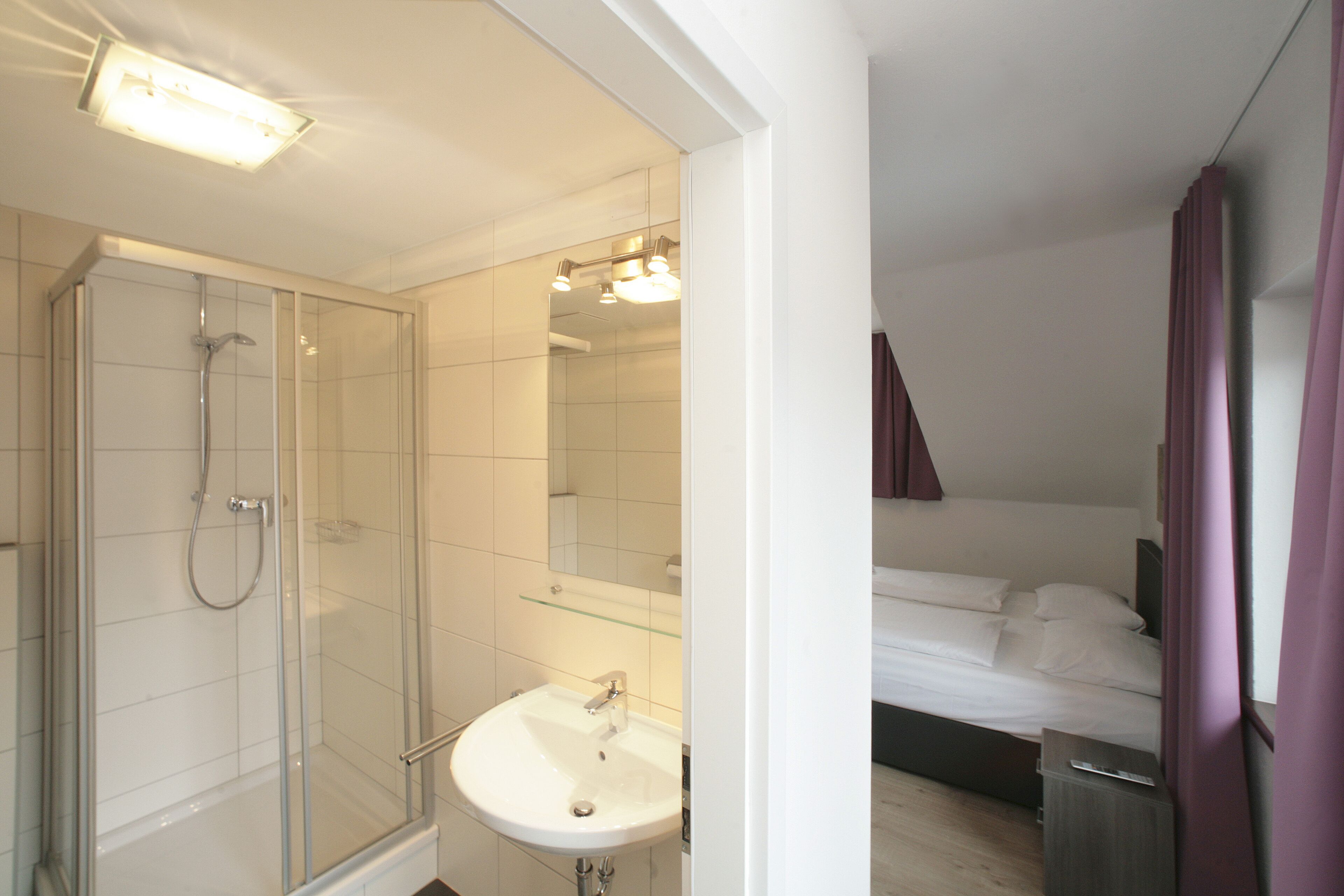 Une salle de bain moderne avec une douche à l’italienne en verre, un lavabo blanc et un miroir au-dessus.