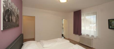 Ein Hotelzimmer mit einem Bett, einem Bild an der Wand, einem Fenster mit Vorhängen und einer Heizung.
