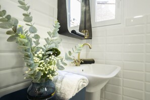 A bathroom with a white sink, a gold faucet, and a vase with white flowers and green leaves.