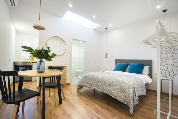A modern bedroom with a bed, a dining table with chairs, a hanging light fixture, and a skylight.