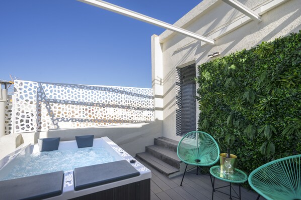 A rooftop terrace with a hot tub, two chairs, and a lush green wall.