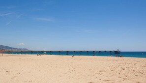 A beach with a pier extending into the water, sandy beach, and clear blue sky.