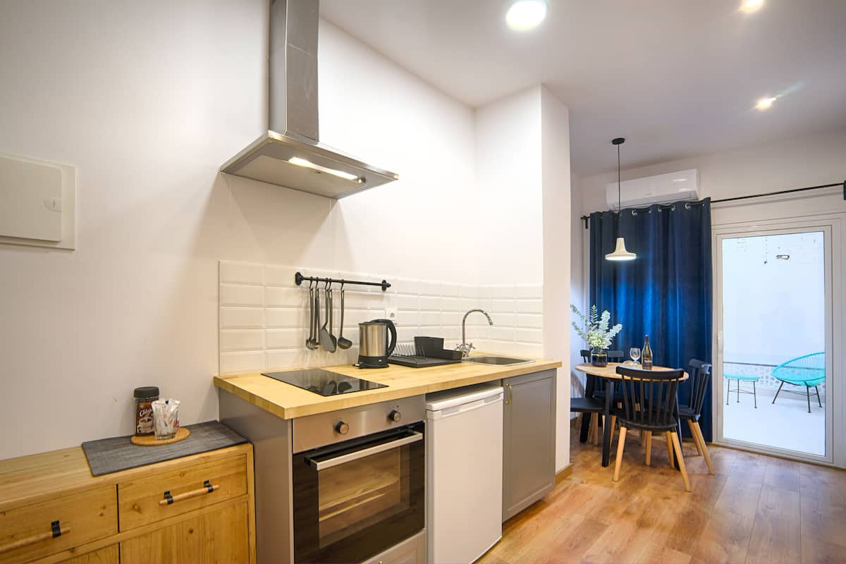 Cozinha moderna com bancada de madeira, eletrodomésticos de aço inoxidável e vista para uma varanda com cortinas azuis.